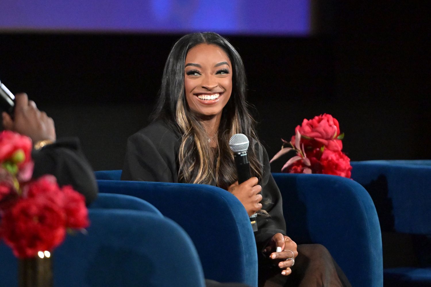 Simone Biles souriante et tenant un micro
