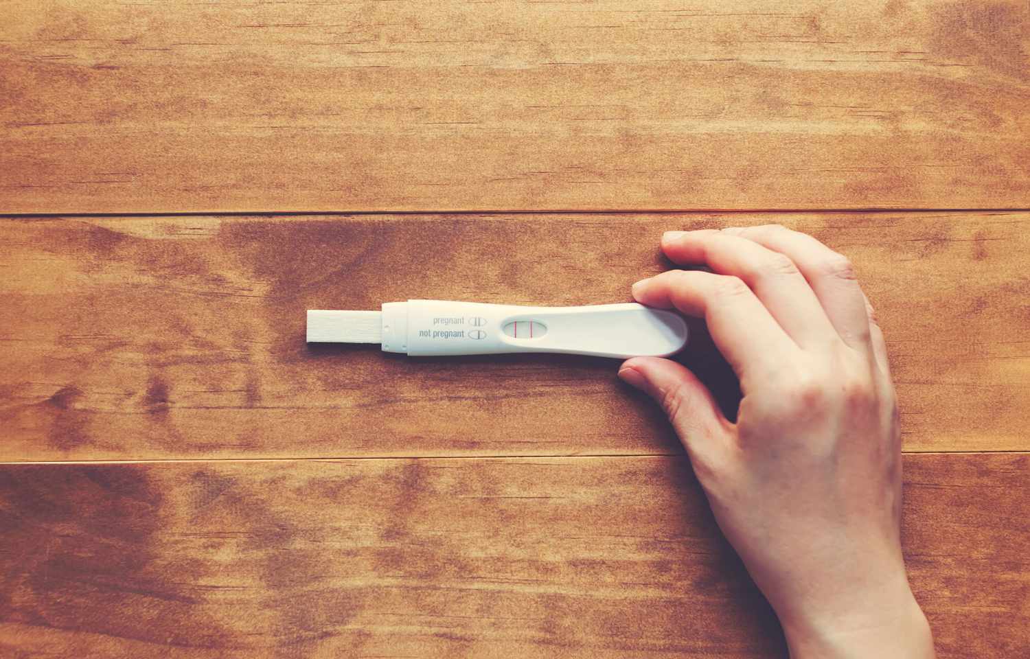 Main tenant un test de grossesse positif sur une table en bois